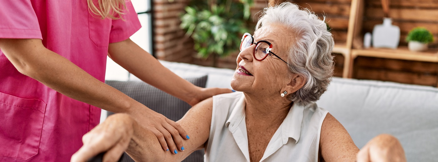 Elderly woman happily sitting on the couch next to her smiling caregiver
