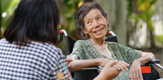 Elderly woman smiling in her wheelchair and receiving assistance from another person