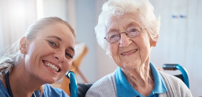 Elderly woman smiling and sitting in a wheelchair alongside her smiling doctor