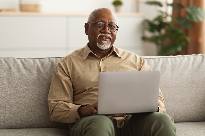 Man grinning while sitting on the couch with his laptop open on his lap