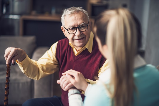 Elderly and disabled man in wheelchair scrolling on phone and sharing a laugh with a nearby young woman sitting next to him